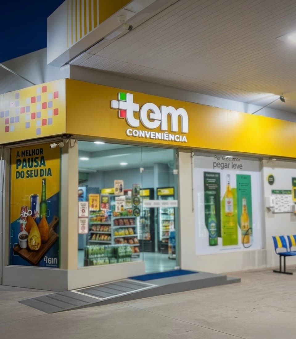 Fachada de uma loja Tem Conveniência iluminada à noite
